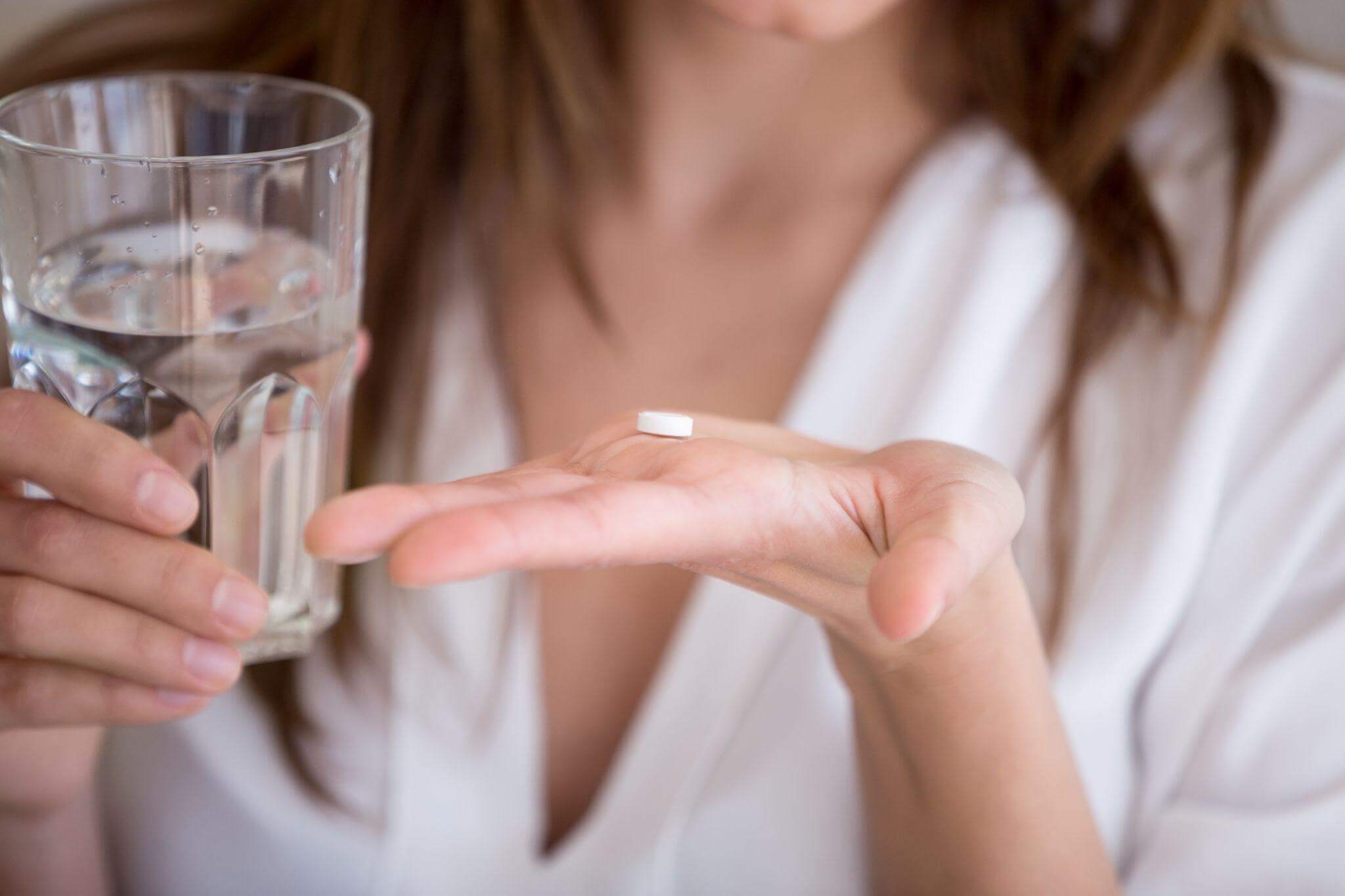 Woman holding up a pill and a glass of water